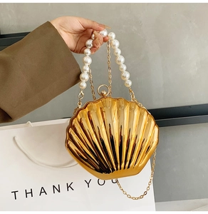 Detail view of a shell-shaped gold metal bag with faux pearl handle and gold chain strap