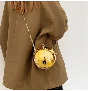 Detail of a spherical gold mirror handbag with a metallic chain on an olive blazer