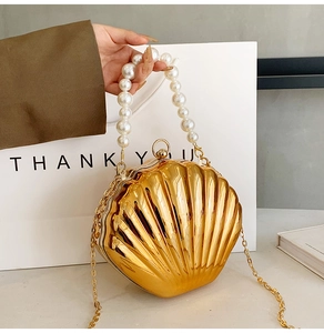 Detail of golden shell-shaped evening clutch bag with pearl handle and metal chain