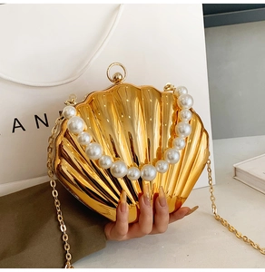 Detail of golden shell-shaped evening bag with pearl handle and metal chain strap