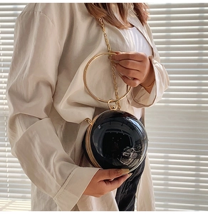 Detail of high-gloss black sphere evening bag with golden ring handle and chain