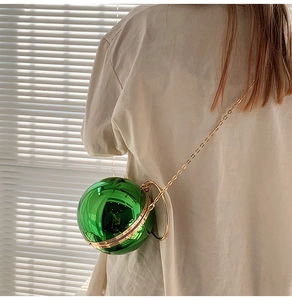 Dettaglio borsa a sfera verde smeraldo con manico ad anello dorato e catena sottile