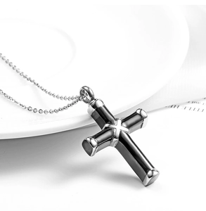 Polished black and silver stainless steel cross urn pendant on a white ceramic plate