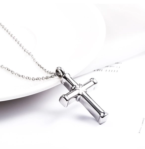 Polished stainless steel cross pendant urn necklace on a white ceramic plate