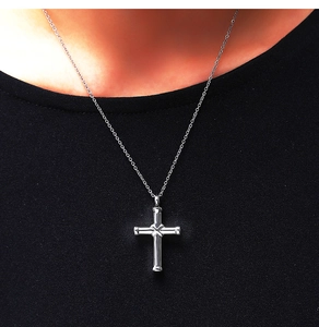 Close-up of a silver stainless steel cross cremation pendant worn on a black outfit