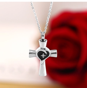 Dettaglio del ciondolo a croce argento con cuore nero su sfondo di rose rosse