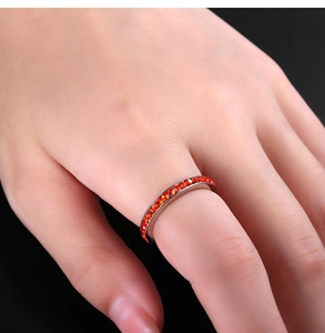 Macro shot of a silver band ring set with vibrant orange cubic zirconia stones on a finger