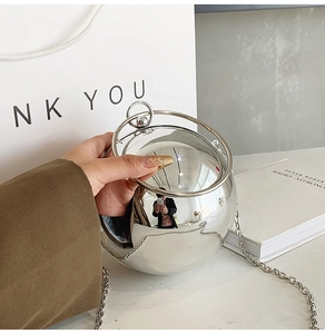 Dettaglio di una borsa sferica a specchio argento con manici ad anello e catena sottile