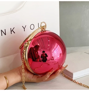 Close-up of sphere evening bag in rose red with gold ring handle and chain strap