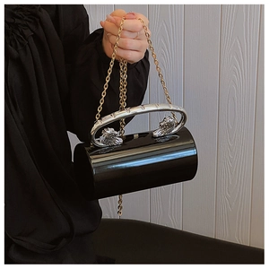 Detailed macro of a black cylindrical evening bag with silver lion head handle and gold chain