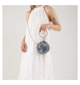 Close-up of circular evening bag featuring gold metal handle and denim textured finish