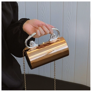 Close-up of golden cylindrical evening bag with silver lion head handles and chain