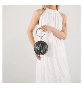 Detail of glittery spherical evening bag with golden ring handle held by a model
