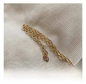 Close-up of the elegant polished golden metal chain strap on a soft beige knit fabric