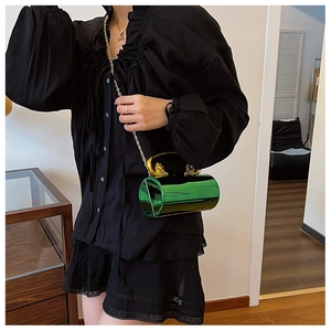 Detail of emerald green cylindrical evening bag with gold lion head handles and chain strap
