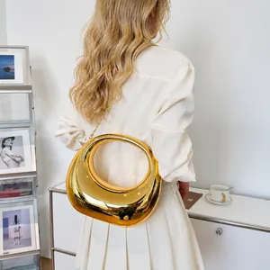 Detalle de bolso de media luna dorado con efecto espejo y correa de cadena metálica