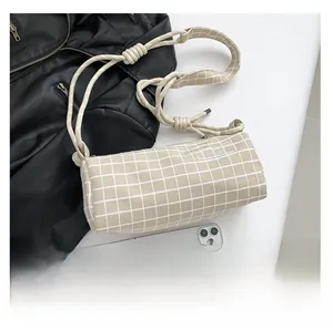 Détail du sac cylindrique à carreaux blanc crème avec bandoulière tressée et étiquette