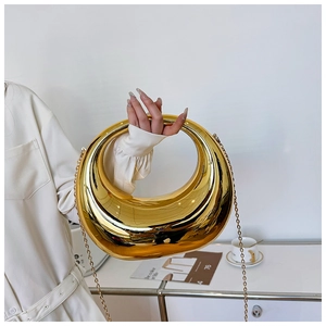 Detalle de bolso de noche dorado con forma de medialuna, acabado espejo y asa circular