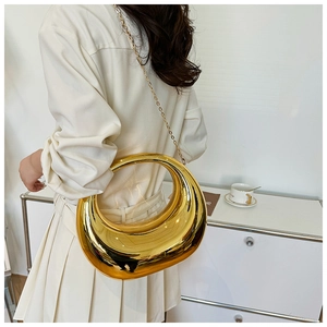 Primer plano de un bolso de media luna dorado con acabado espejo y cadena en modelo