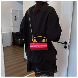 Detail of red cylindrical acrylic bag with gold lion head handles and chain strap