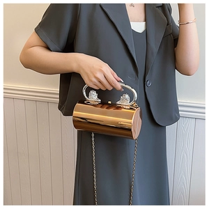 Detail of rose gold cylindrical clutch with dual lion head handles and chain strap