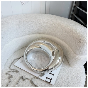 Detalle del bolso de noche plateado en forma de luna sobre sillón blanco suave