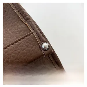 Macro detail of dark brown lychee grain leather with precise stitching and silver rivet
