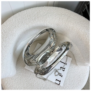 Detalle del bolso medialuna plateado con anillos huecos sobre un sofá de lana blanca