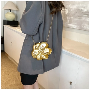 Detail of flower-shaped golden evening bag with metallic mirror finish and chain
