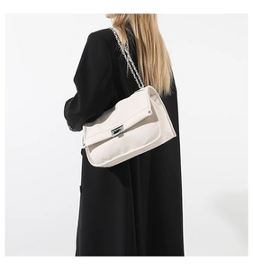 Close-up of beige leather messenger bag with silver chain and litchi texture on black coat