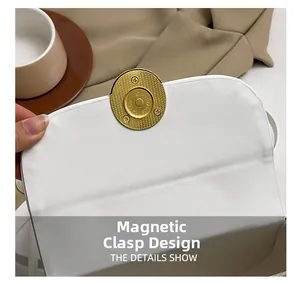 Detailed view of the gold magnetic clasp on a white leather minimalist handbag