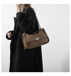 Detailed shot of brown litchi pattern leather messenger bag with silver twist lock on coat
