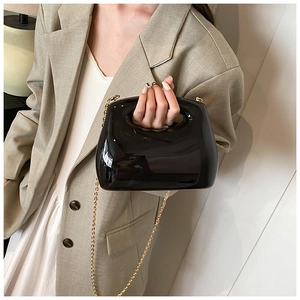 Detail of black patent leather handbag with round handle and gold chain strap on model