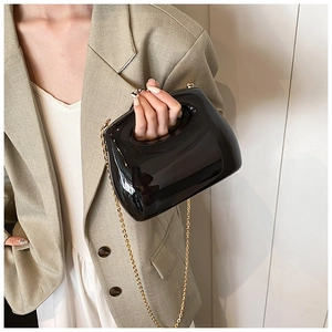Chic black acrylic sculptural handbag with gold chain strap shown on beige blazer