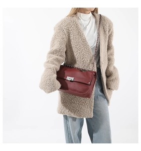 Detail of wine red pebble leather messenger bag with silver lock on beige coat outfit
