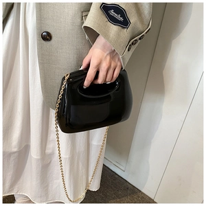 Detail of a black glossy acrylic clutch bag with a sleek hollow handle and gold chain strap
