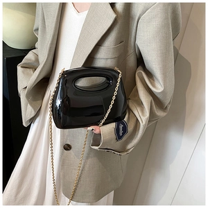 Detail of glossy black acrylic handbag with oval cutout handle and gold chain strap