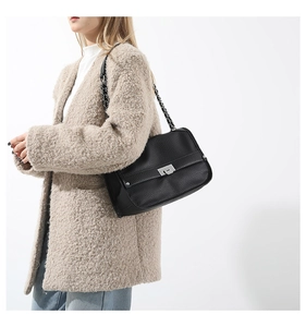 Detail of black pebbled leather messenger bag featuring silver metal turn-lock and chain strap