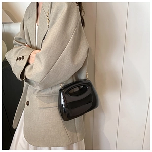 Detailed view of a black acrylic handbag with a gold chain strap and glossy finish