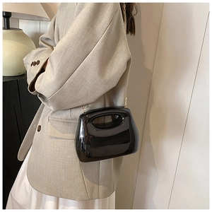 Detail of glossy black acrylic handbag with gold chain strap on beige blazer outfit