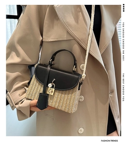 Dettaglio della borsa in paglia intrecciata con patta in pelle nera e fibbia a fiore