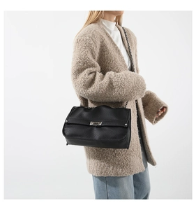 Detail of black pebbled leather crossbody bag with silver clasp worn on beige coat