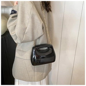 Detail of glossy black acrylic evening bag with a delicate gold chain shoulder strap