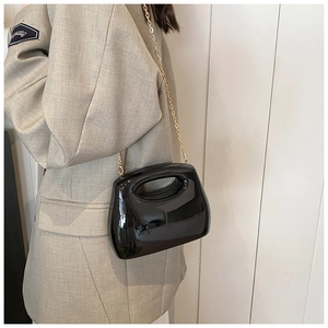 Detail view of a black glossy acrylic clutch bag with a gold chain strap and mirror finish