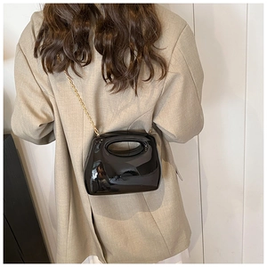 Glossy black acrylic handbag with gold chain strap shown being worn with a beige blazer