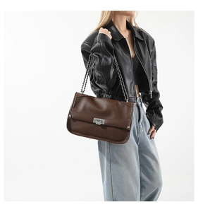 Close-up of dark brown leather messenger bag with silver chain strap on model