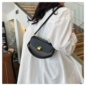 Detail of half-moon shoulder bag with golden spherical lock worn by model in white shirt