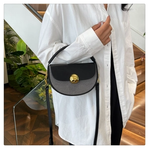 Detail of a half-moon saddle bag featuring a bold gold orb lock and chic mixed texture design