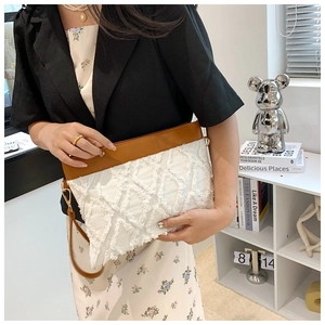 Détail d'une pochette blanche à pompons avec garniture en cuir brun et zip doré
