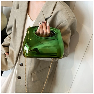 Detail view of glossy green acrylic clutch bag with golden chain on beige suit